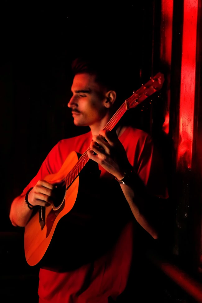 JHACA tocando violão sob luz vermelha.